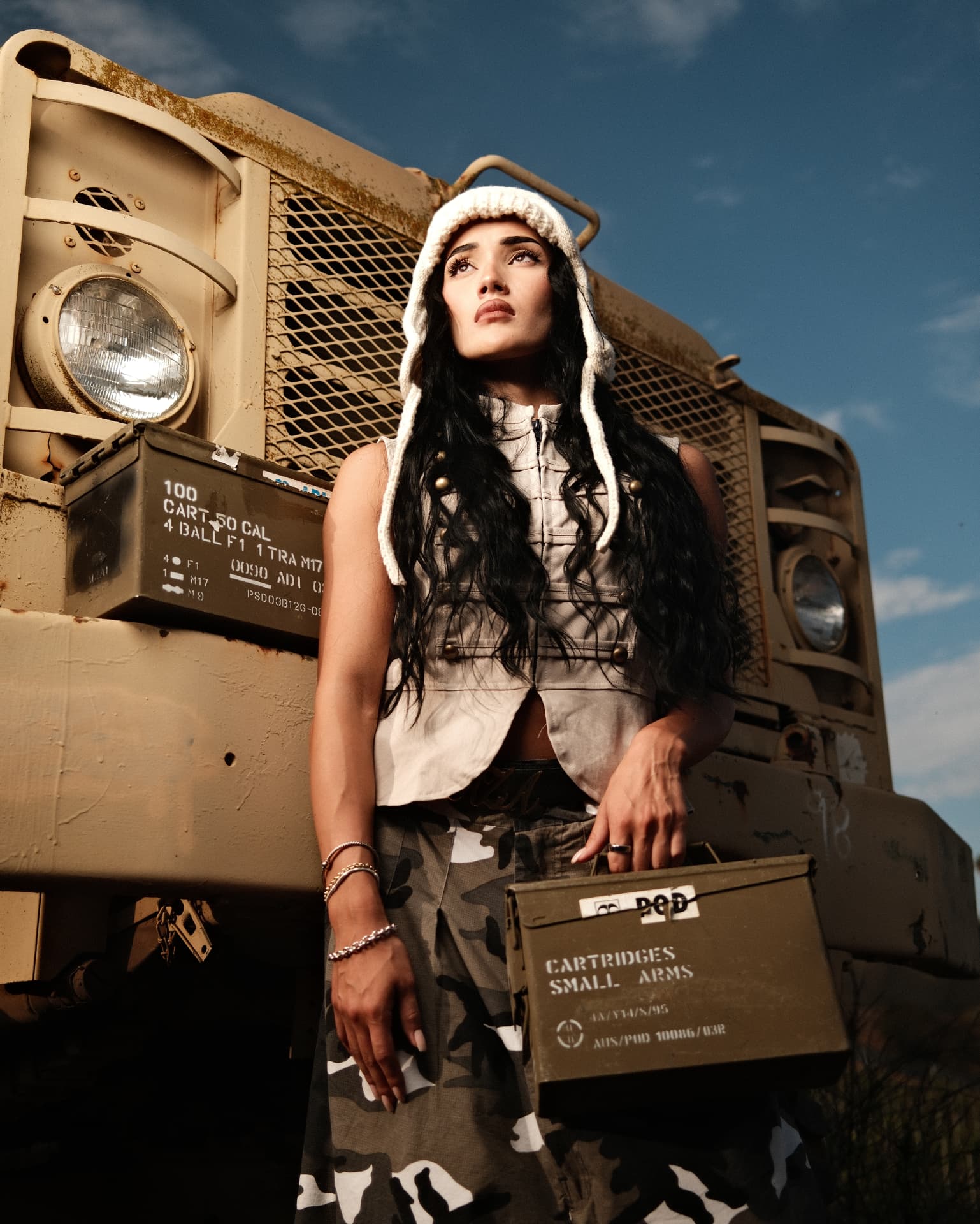 Portrait in a knit hood holding an ammo box in front of a military truck