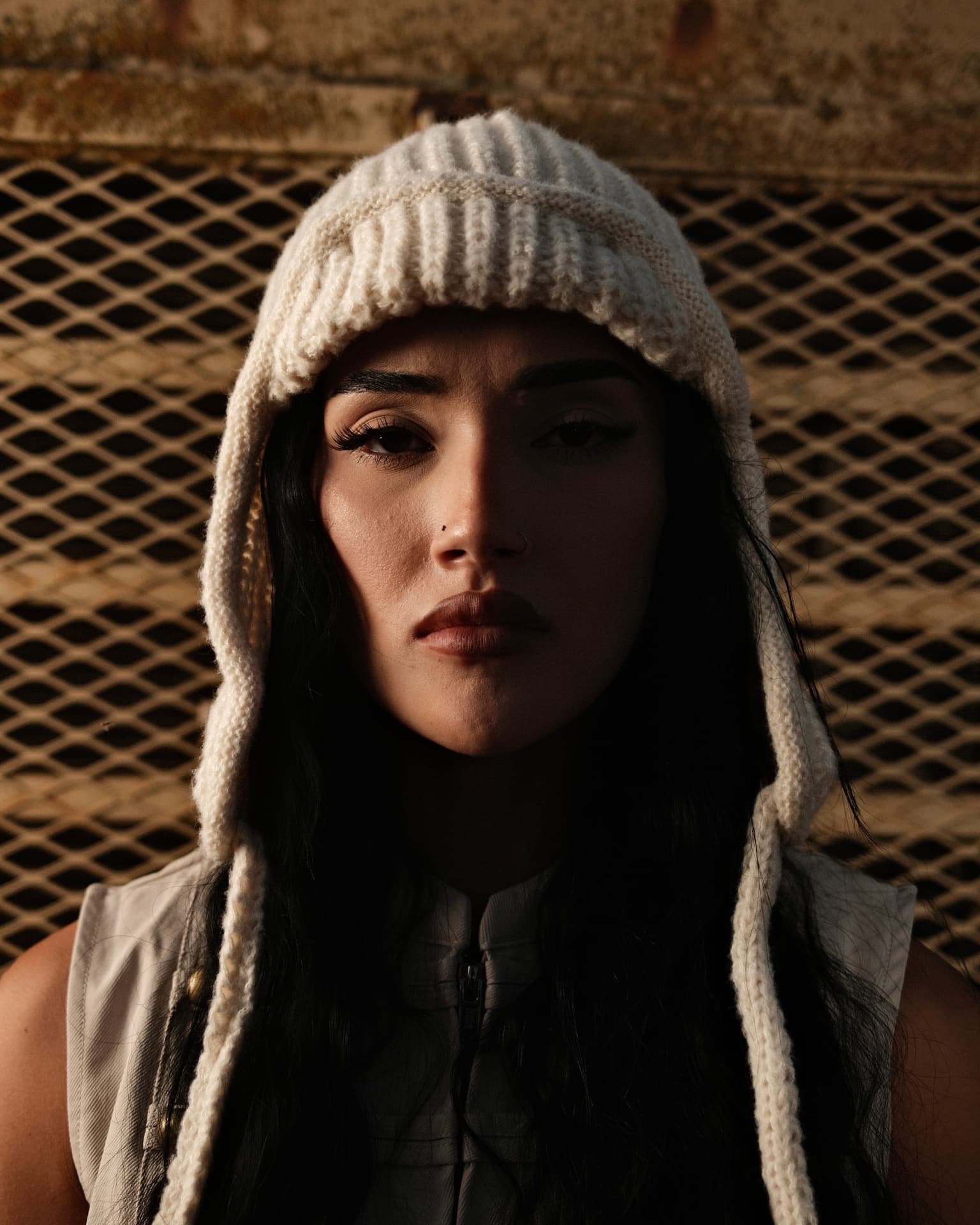 Close portrait in a white knit hood against a metal mesh background