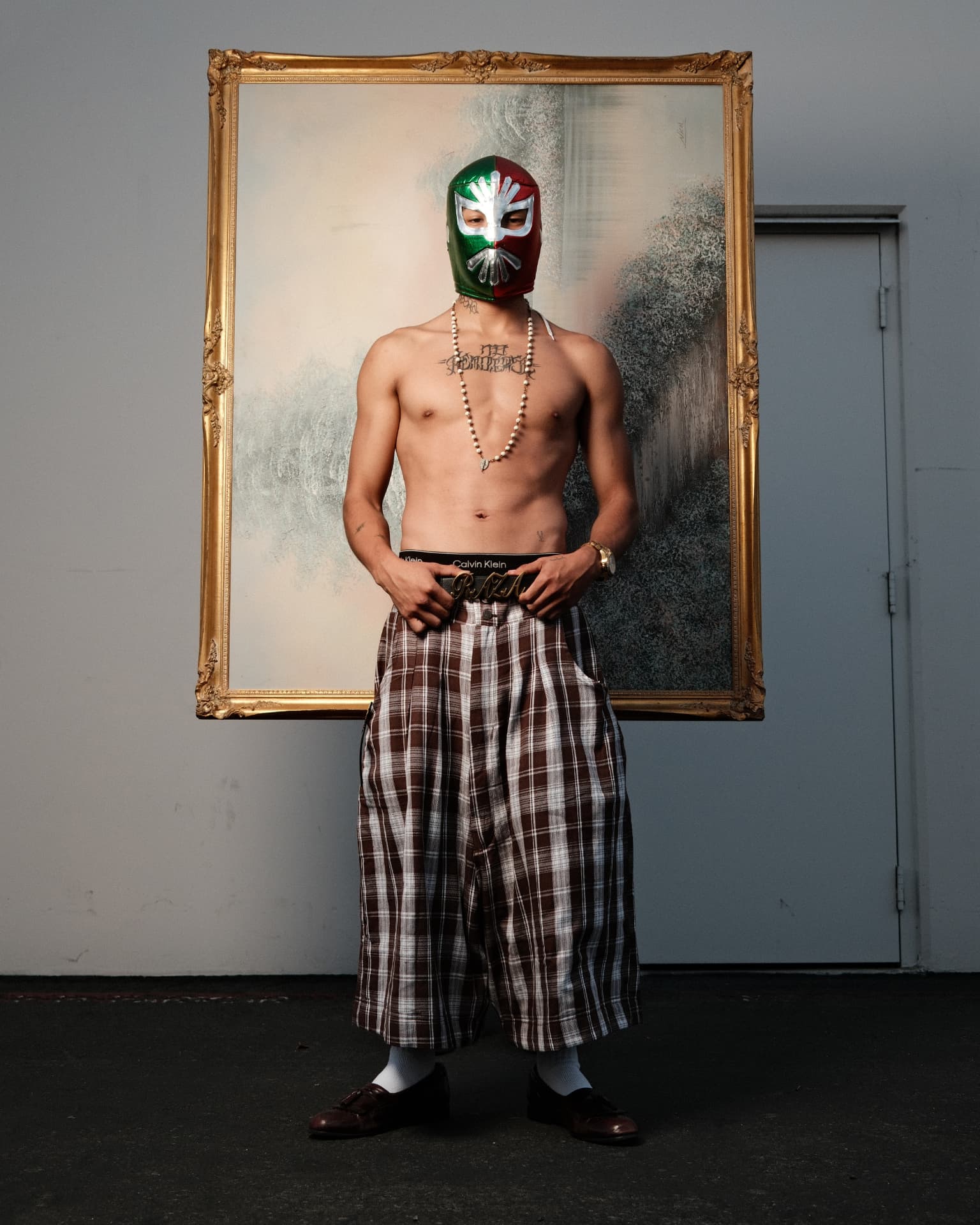 Masked figure standing before a gilded framed painting outdoors